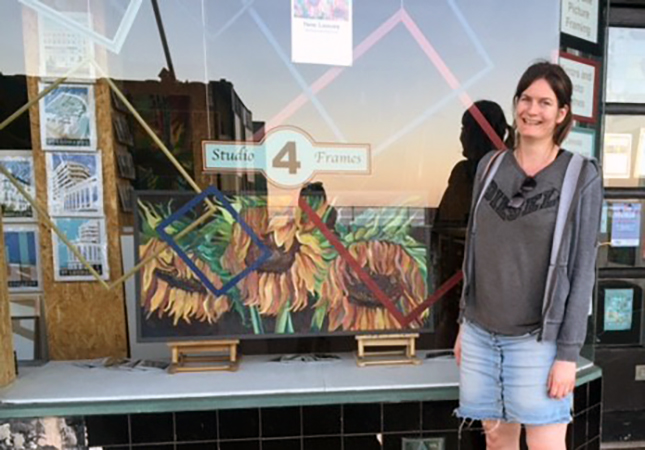 Emily Gray in front of shopfront with her framed paintings