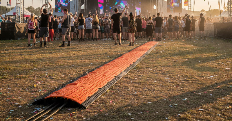 Protector de cable Orange Cross 3 sobre el c&eacute;sped en un festival frente a una multitud que observa el escenario.
