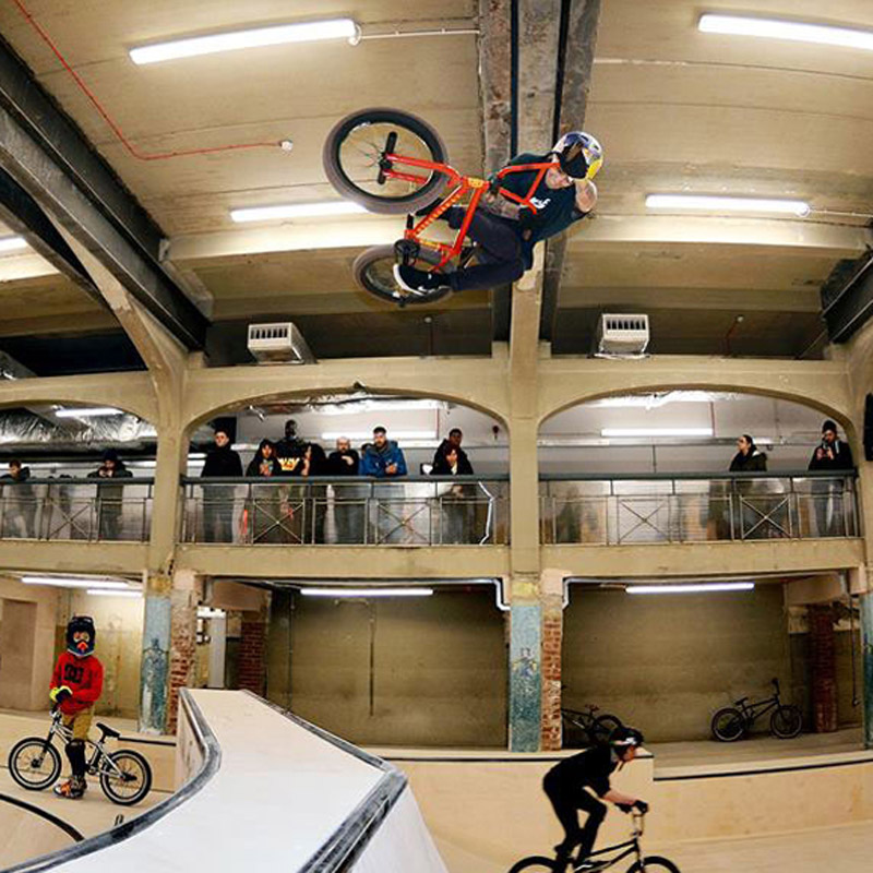 Action shot at Source BMX Skate Park of person mid-air on a bike with people watching 